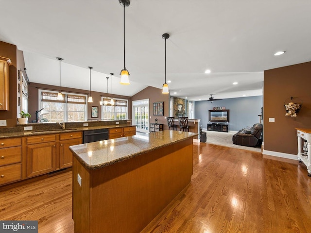 kitchen featuring a center island, dishwasher, dark stone counters, light wood-type flooring, and brown cabinets