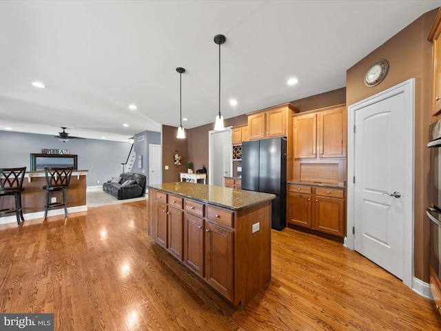 kitchen featuring dark stone countertops, wood finished floors, a center island, freestanding refrigerator, and recessed lighting