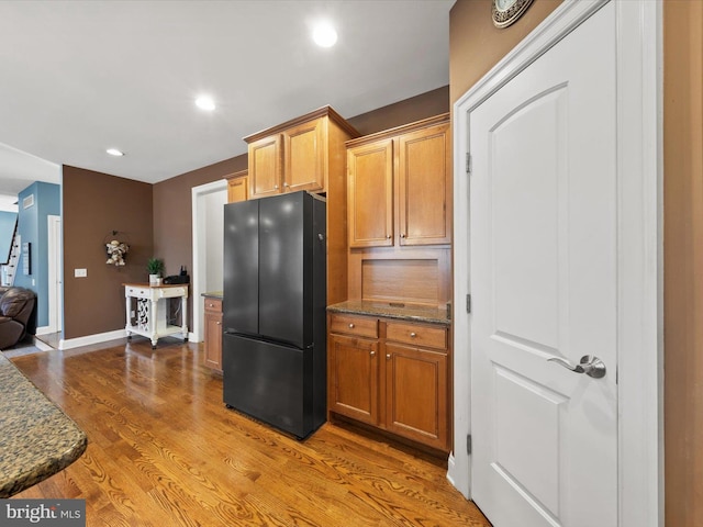 kitchen with baseboards, recessed lighting, dark stone countertops, freestanding refrigerator, and light wood-style floors