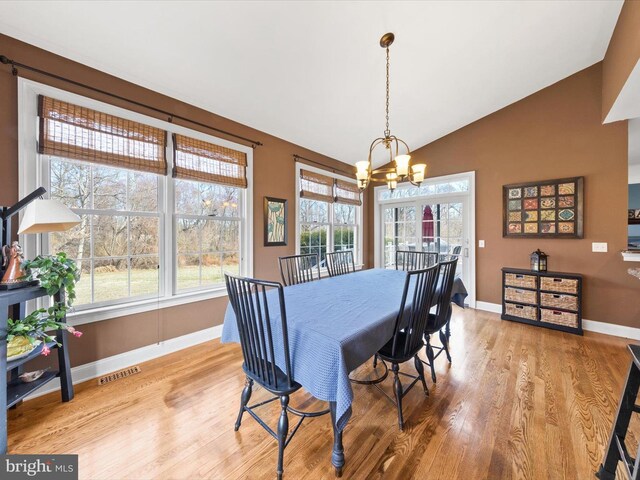 dining space featuring wood finished floors, visible vents, baseboards, lofted ceiling, and a notable chandelier