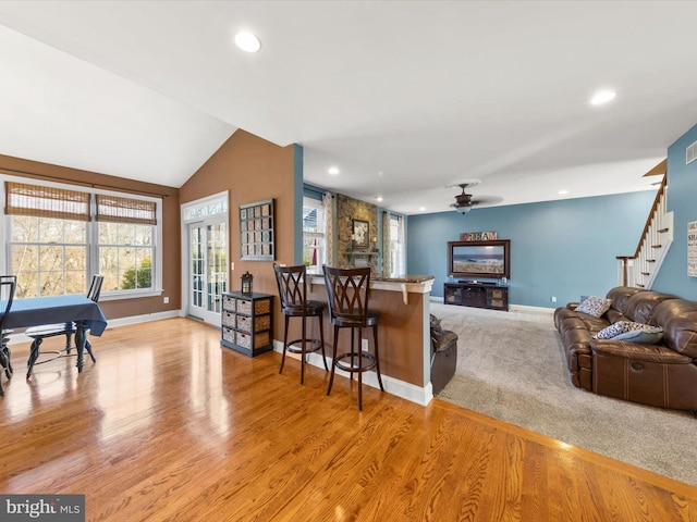 interior space with a breakfast bar area, baseboards, lofted ceiling, light wood-style floors, and open floor plan