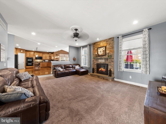 carpeted living area with a stone fireplace, plenty of natural light, visible vents, and a ceiling fan