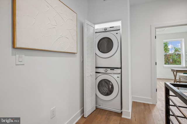 clothes washing area featuring wood-type flooring and stacked washer / dryer