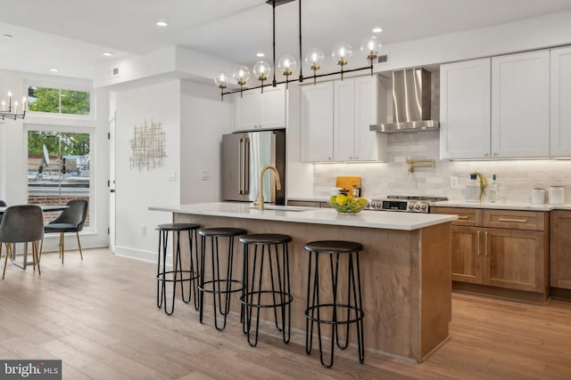 kitchen with white cabinetry, wall chimney range hood, high quality fridge, and a center island with sink