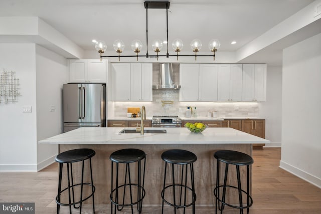 kitchen featuring appliances with stainless steel finishes, sink, wall chimney range hood, and a kitchen island with sink