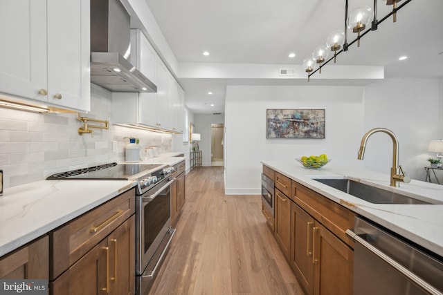 kitchen with wall chimney exhaust hood, sink, white cabinetry, appliances with stainless steel finishes, and light stone countertops