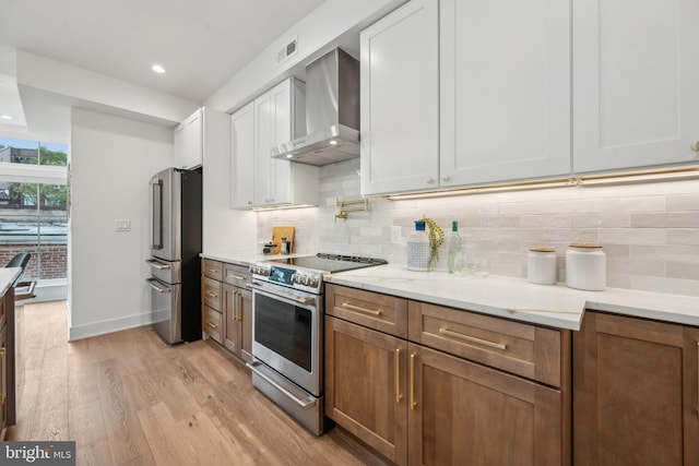 kitchen featuring wall chimney exhaust hood, white cabinetry, tasteful backsplash, appliances with stainless steel finishes, and light hardwood / wood-style floors