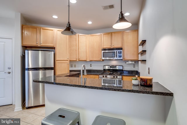 kitchen with dark stone counters, stainless steel appliances, light brown cabinetry, pendant lighting, and light tile patterned flooring