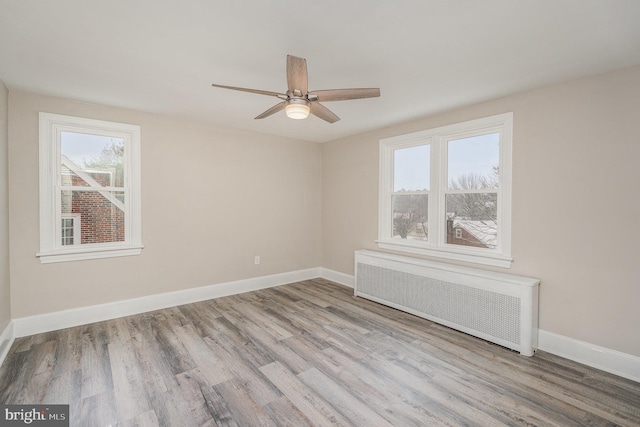 empty room featuring ceiling fan, radiator heating unit, plenty of natural light, and light hardwood / wood-style flooring