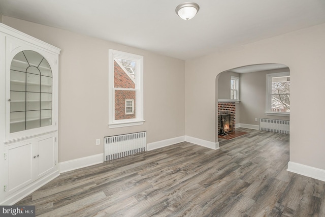 spare room with radiator, a brick fireplace, and hardwood / wood-style flooring