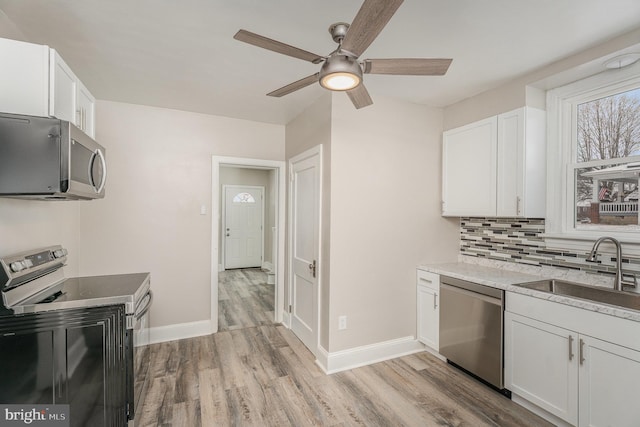 kitchen with light wood-type flooring, stainless steel appliances, backsplash, sink, and white cabinetry