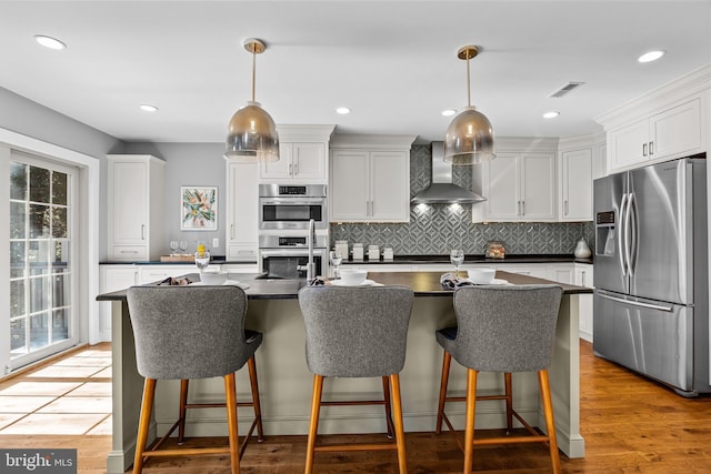 kitchen with white cabinetry, appliances with stainless steel finishes, pendant lighting, and wall chimney range hood