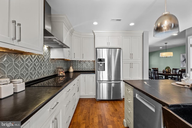 kitchen featuring stainless steel appliances, white cabinetry, wall chimney range hood, and decorative light fixtures