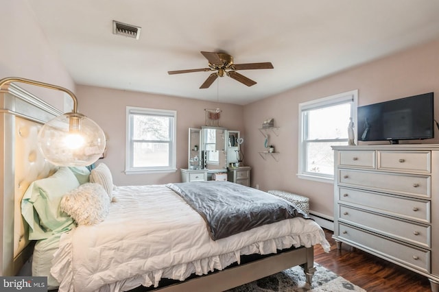 bedroom featuring multiple windows, visible vents, baseboard heating, and dark wood-style flooring