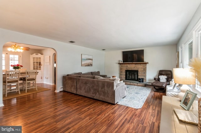 living room featuring arched walkways, a stone fireplace, a notable chandelier, visible vents, and dark wood-style floors