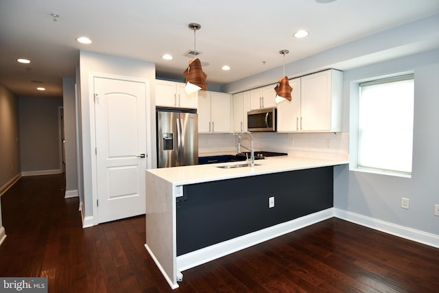 kitchen with stainless steel appliances, a peninsula, a sink, light countertops, and decorative light fixtures