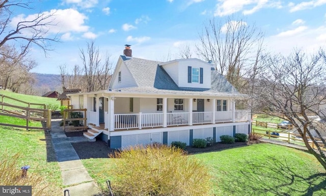 country-style home featuring covered porch, a shingled roof, fence, a chimney, and a front yard