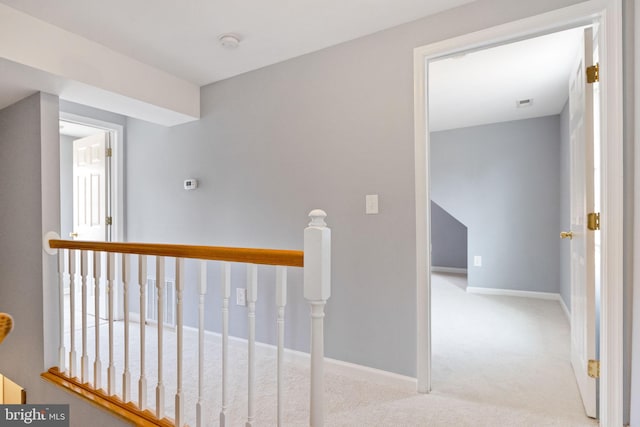 corridor featuring carpet floors, visible vents, baseboards, and an upstairs landing