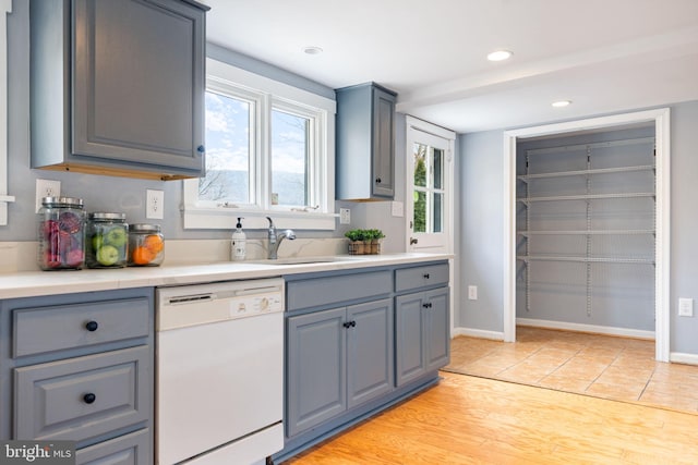 kitchen with light countertops, white dishwasher, a sink, and gray cabinetry