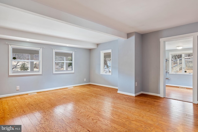 unfurnished room with visible vents, beamed ceiling, light wood-style flooring, and baseboards