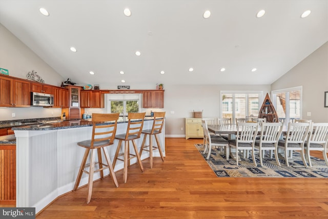 kitchen featuring light wood-type flooring, a wealth of natural light, stainless steel microwave, and a kitchen bar