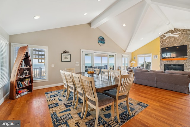 dining room featuring high vaulted ceiling, a fireplace, baseboards, light wood-type flooring, and beamed ceiling