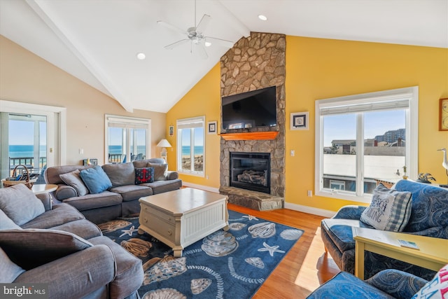 living area featuring baseboards, ceiling fan, beamed ceiling, wood finished floors, and a stone fireplace