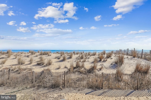 water view featuring fence and a beach view