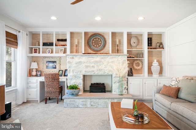 carpeted living area with a stone fireplace, recessed lighting, and built in features