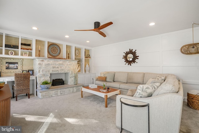 carpeted living room with ceiling fan, built in shelves, recessed lighting, a decorative wall, and a fireplace