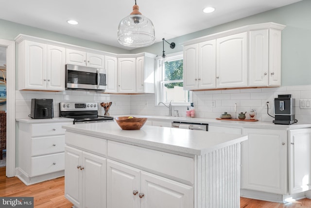 kitchen with light wood finished floors, white cabinets, a kitchen island, appliances with stainless steel finishes, and decorative light fixtures