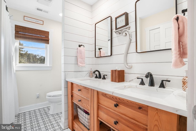 bathroom featuring baseboards, a sink, toilet, and double vanity