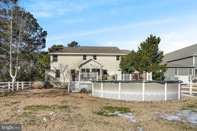 rear view of property featuring a deck, fence, and a covered pool