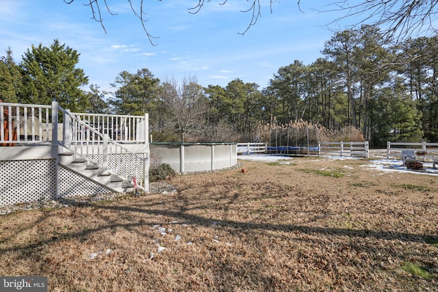 view of yard featuring a trampoline, a covered pool, fence, and a wooden deck