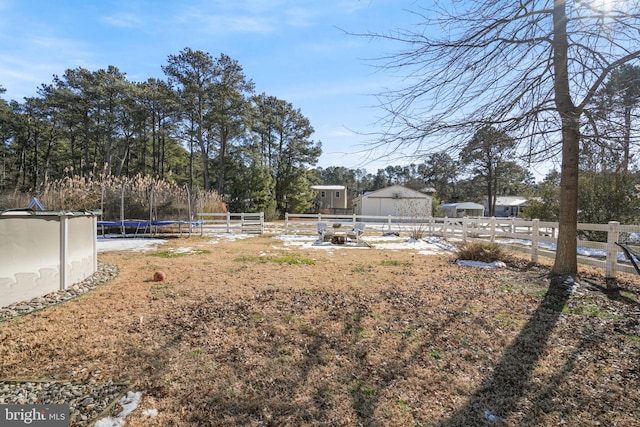 view of yard with a trampoline, fence, and an outbuilding