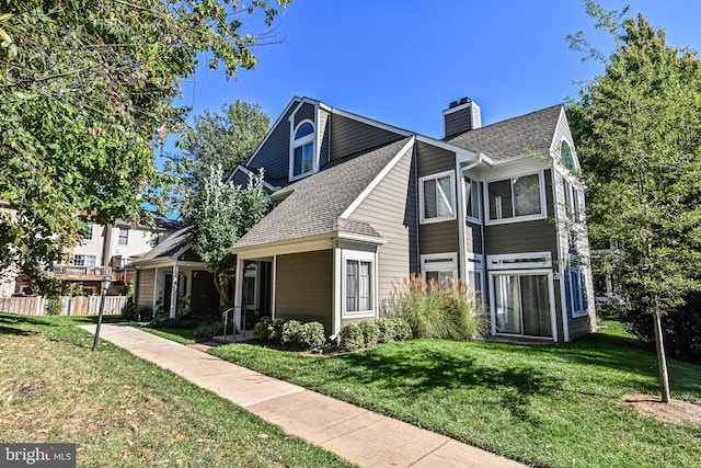 view of front of home featuring roof with shingles, a chimney, and a front yard