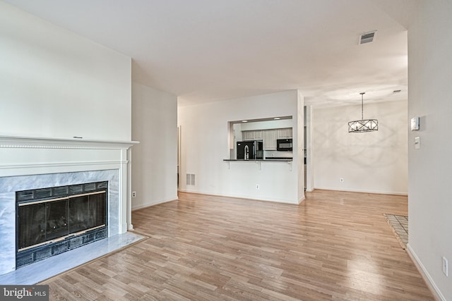 unfurnished living room featuring visible vents, a fireplace, a notable chandelier, and light wood finished floors