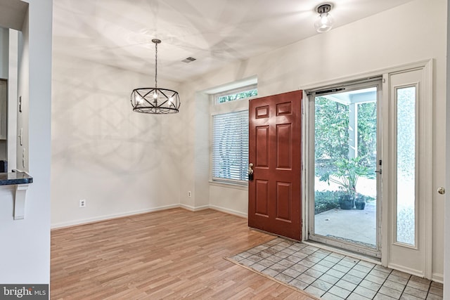 entrance foyer with a healthy amount of sunlight, light wood-style flooring, a chandelier, and baseboards