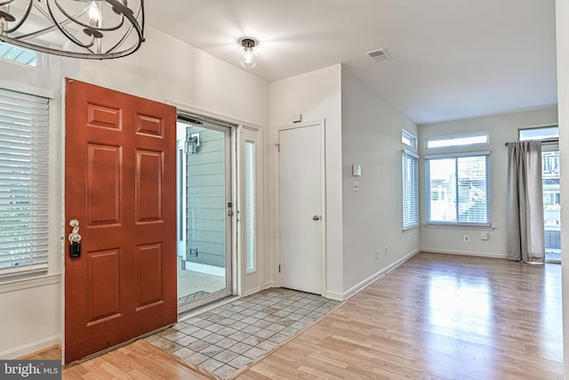 entryway with baseboards, an inviting chandelier, visible vents, and light wood-style floors