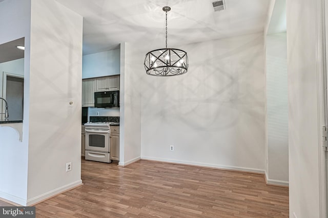 unfurnished dining area with a notable chandelier, lofted ceiling, visible vents, wood finished floors, and baseboards