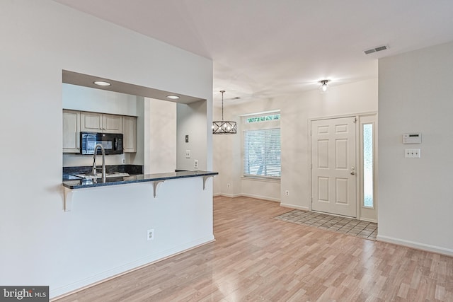 kitchen featuring black microwave, a sink, visible vents, a kitchen breakfast bar, and decorative light fixtures