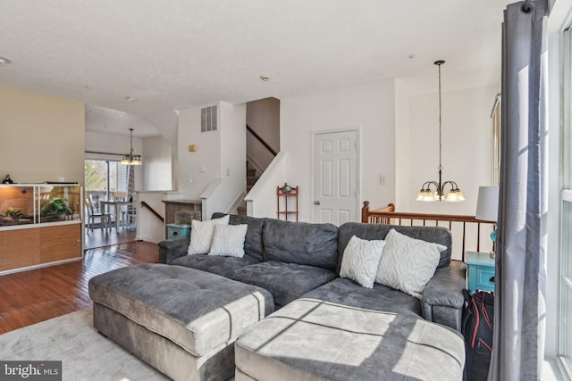 living room featuring a chandelier, visible vents, stairs, and wood finished floors