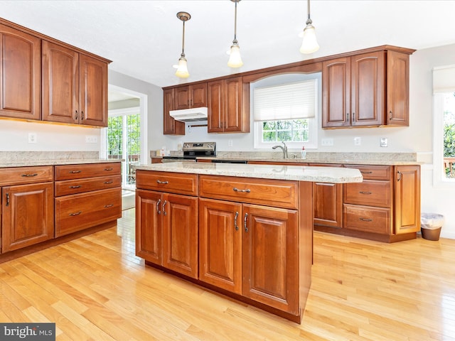 kitchen with a sink, stainless steel range with electric cooktop, pendant lighting, light wood finished floors, and under cabinet range hood