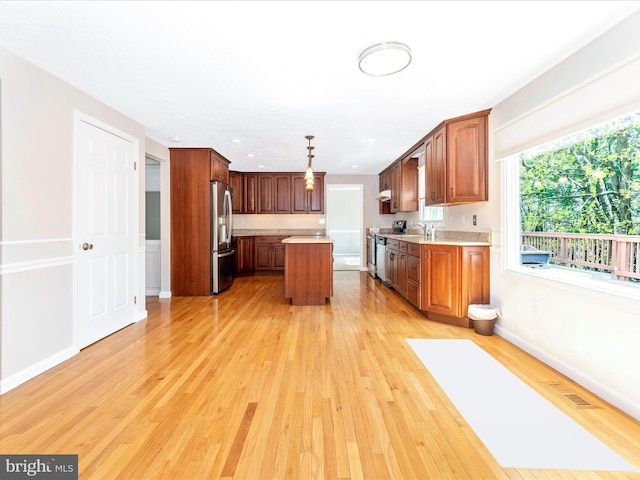 kitchen with a sink, light countertops, light wood-style flooring, appliances with stainless steel finishes, and a kitchen island