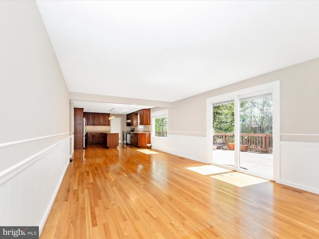 unfurnished living room with light wood-type flooring, a wainscoted wall, and visible vents
