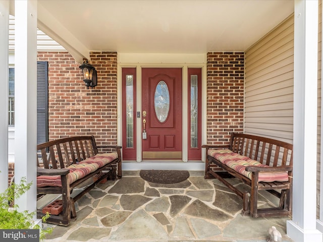 view of exterior entry featuring brick siding and covered porch