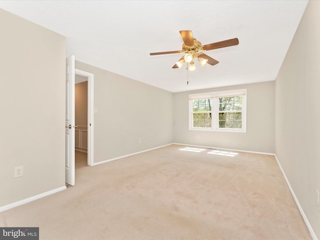 spare room with a ceiling fan, baseboards, and light colored carpet