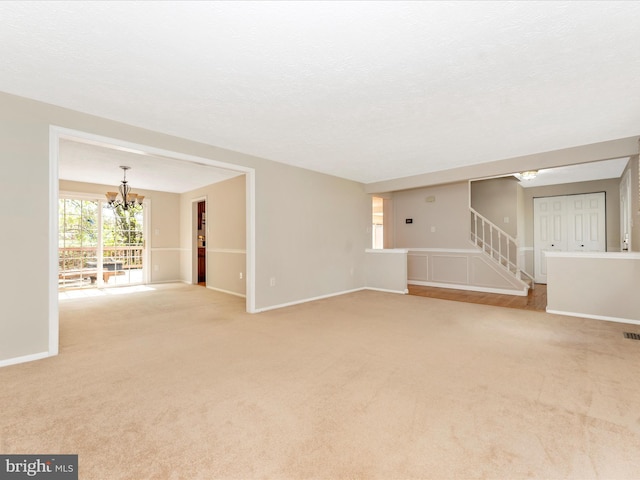 unfurnished living room with light carpet, visible vents, baseboards, a notable chandelier, and stairway