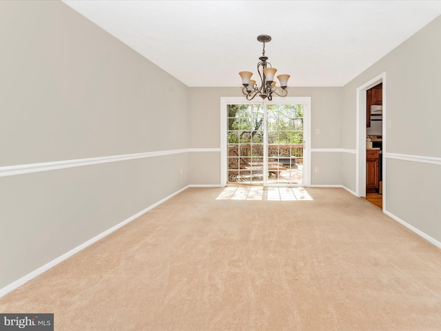 spare room featuring baseboards, an inviting chandelier, and light carpet