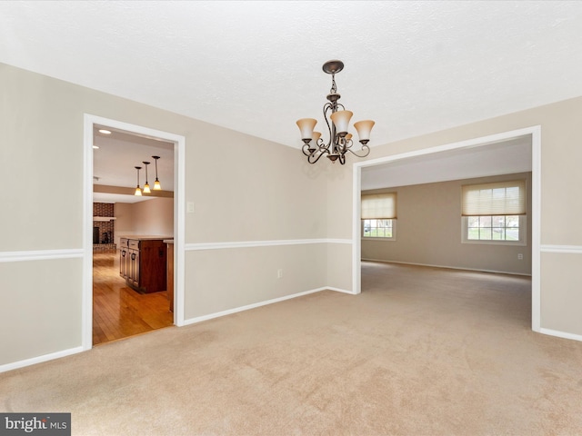 spare room with light carpet, baseboards, and an inviting chandelier